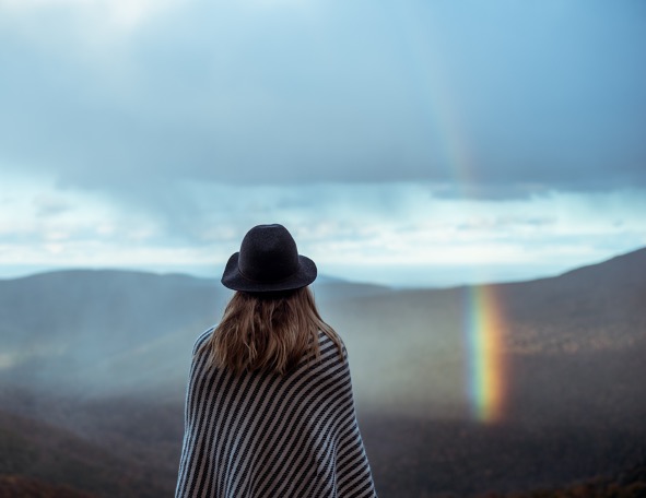 bildet viser en dame med hatt som ser på regnbuen